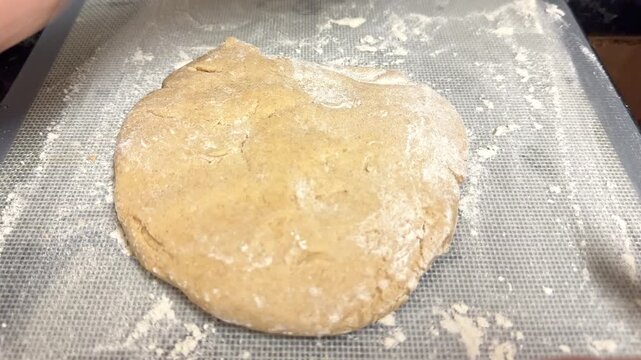 Close up of a woman using a wooden rolling pin to flatten a ball of cookie raw dough on a baking mat