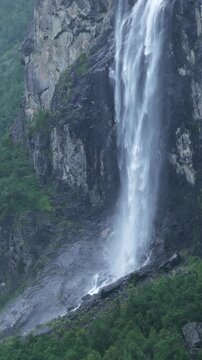 backward drone flight, View on big waterfall in Romsdalen valley, falling from a high cliff, during rainy day in summer. Steep mountain cliffs, rocks, pristine forest. Amazing wilderniss in Norway. Re