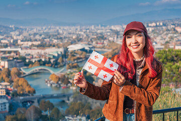 Cheerful woman holding a Georgia flag enjoying the panoramic view of Tbilisi cityscape and the Kura River