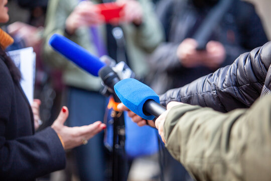 Journalists holding microphones toward spokesperson during outdoor press interview, media coverage, breaking news, public statement, journalism and political communication concept