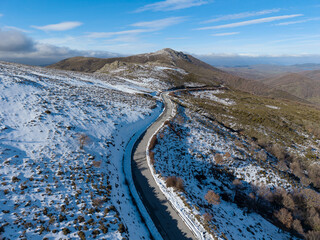 Drone view of a winding mountain road surrounded by snow under a blue sky