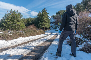 Man Seen from Behind Standing on Snowy Mountain Road Under Blue Sky