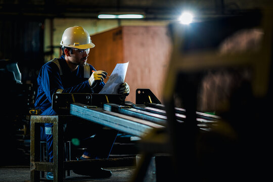 Industrial worker measuring a metal component in a factory workshop while wearing safety helmet and gloves, ensuring precision, quality control, and workplace safety in manufacturing process.