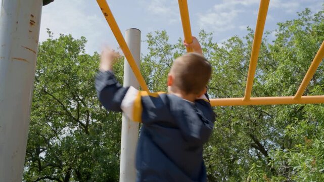 Perspective shot of a child moving along yellow monkey bars at a park. Dynamic angle showing the sky through the bars, green trees on the sides.