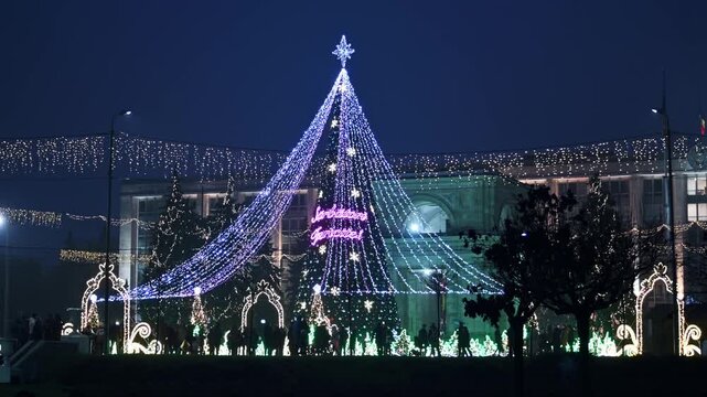 Beautifully decorated Christmas tree and buildings with lights at night, people celebrating holidays