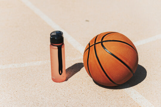 Basketball ball and plastic bottle with water on court. Summer outdoors activity.