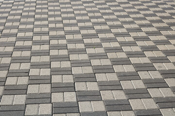 Fototapeta premium Closeup of interlocking cream and grey paving stones forming a repeating geometric pattern, creating a clean and orderly outdoor surface.