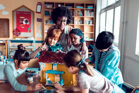 Teacher guiding children painting model house in classroom