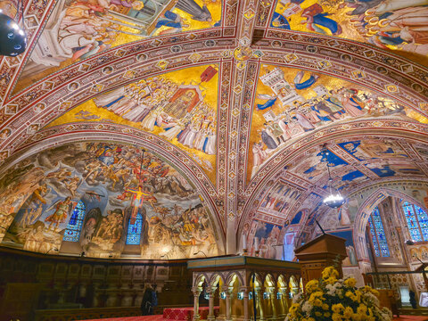 Interior view of the Lower Basilica of San Francesco in Assisi, Italy, featuring ornate frescoed vaults, medieval art masterpieces, and the high altar in a spiritual atmosphere