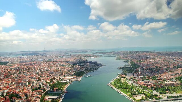 Stunning aerial motion shot reveals istanbul's golden horn cityscape with historic landmarks, lush green spaces, and bustling bridges under a bright blue sky, 