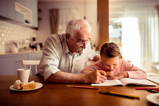 Grandfather helping granddaughter with homework at kitchen table