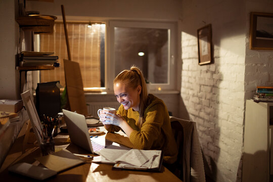Smiling young woman working late at home office on laptop