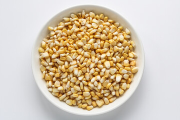 Fototapeta premium Top view of a plate filled with raw corn kernels, isolated on a light background.