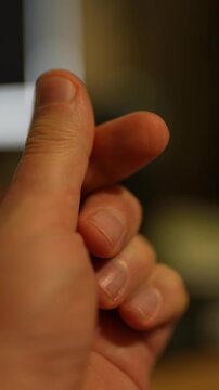 Close-up of a hand making a "finger heart" gesture. Soft, warm lighting illuminates the skin. The background is heavily blurred with dark tones, an out-of-focus white light source