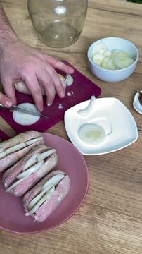 Man slicing a sausage lengthwise. Stuffing it with onion rings and placing it on a saucer. For making pickled sausages. Vertical video.