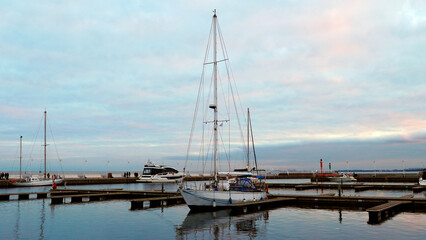 Fototapeta premium Sailboat anchored in harbor with cloudy sky and other boats during sunset