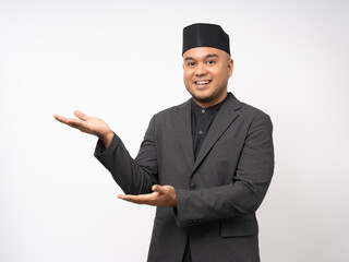 Portrait happy young asian muslim man pointing on isolated white background. Islamic Attractive Muslim man wearing songkok cap islam costume.
