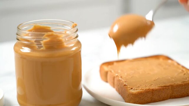 peanut butter jar with spoon spreading on toast, breakfast food, for marketing or recipe use