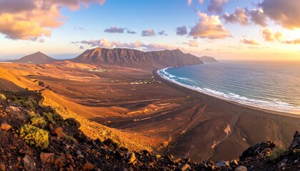 Expansive panoramic view of a coastal landscape at sunset. Sandy beach curves around the bay, with dramatic mountain range in the distance