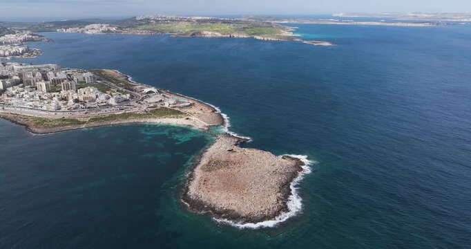 Aerial view of the rocky island and coastal city with buildings surrounded by deep blue water meeting the horizon, St. Paul's Bay, Malta.