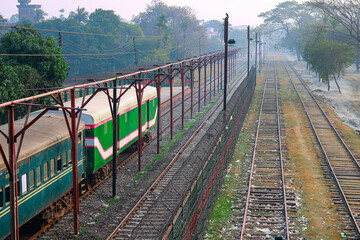 Green and white passenger train parked at a station with multiple railway tracks and misty background.