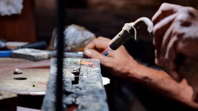 Jeweler soldering metal ring with torch flame on workbench, craftsman hands shaping jewelry in workshop, closeup artisan craftsmanship and handmade production concept
