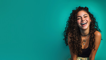 Joyful Latin teen girl portrait with curly hair laughing openly, expressing happiness, individuality, diversity, positive emotions, confidence. Flat turquoise background. Copy space. Banner template.
