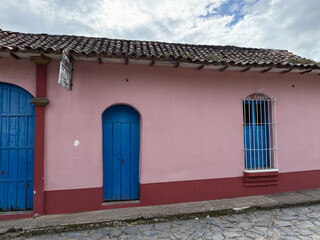 Minimalist exterior of a colorful colonial house facade with pink walls and blue wooden doors
