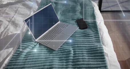 Resting silver laptop showing faint digital grid on bed, with smartphone, teal blanket, tiled floor
