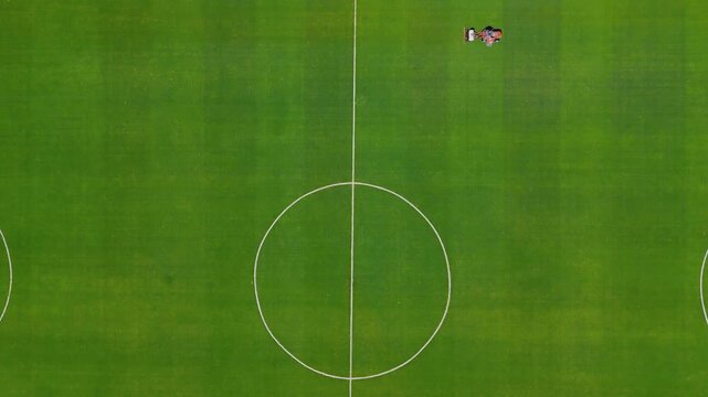 Static overhead view of lawn mower working on Gigante de Arroyito football pitch in Rosario, Argentina. Fixed aerial shot showing grass cutting machine moving across green field from above