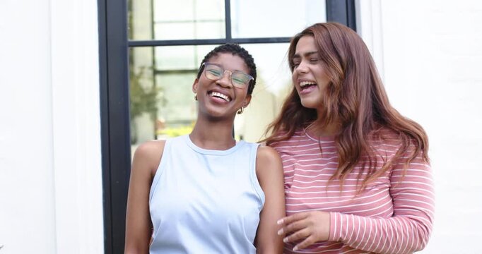 African American friends leaning close laughing, hugging, tucking hair at home's door for camera