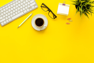 Home office workspace with computer keyboard and cup of coffee on yellow background, top view. Education online. Tabletop of freelancer.