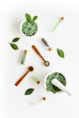 Tea tree essential oil and sea salt near green leaves on white background top view. Organic cosmetics products.