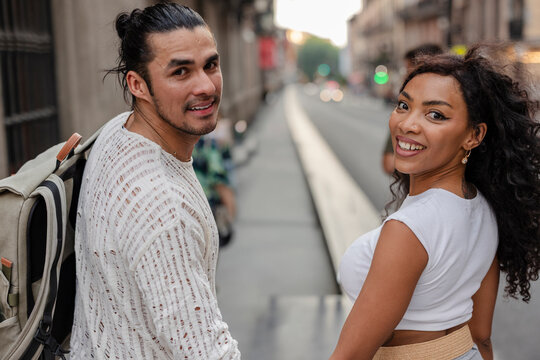 Diverse couple walking city street happily looking back