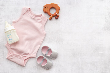 Flat lay of baby bodysuits and eco friendly accessories - booties, wooden rattle toy and baby bottle with milk on gray background, top view