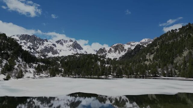 Cinematic aerial drone view of Estany de Ratera in Aiguestortes National Park, snowy Pyrenees mountains in winter landscape