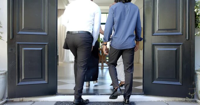Four friends walking into entry after doors open to greet, dressed smartly, hugging near table