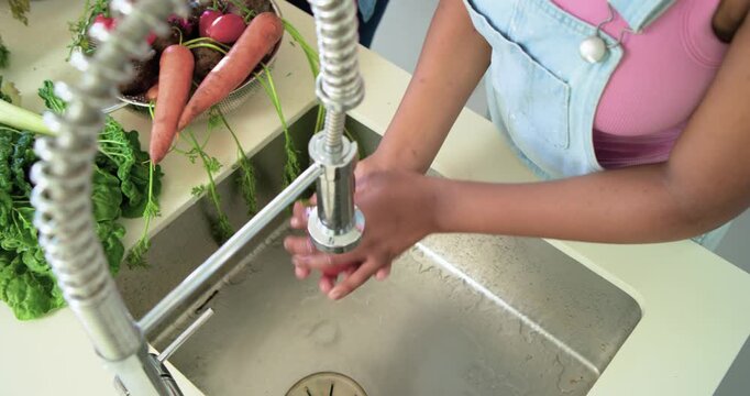 Child is turning faucet handle and rinsing radishes and carrots at kitchen sink while removing dirt