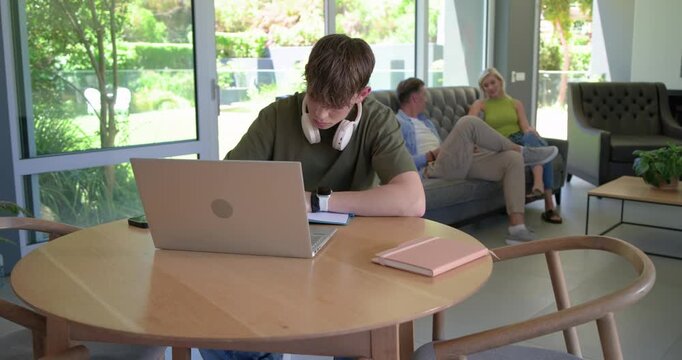 Teenage boy with parents studying at table with silver laptop for homework while camera zooming in