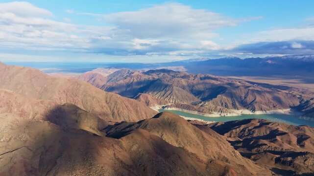 High altitude drone view of vast mountain range reflects in tranquil Orto Tokoy reservoir during daytime in Kyrgyzstan.