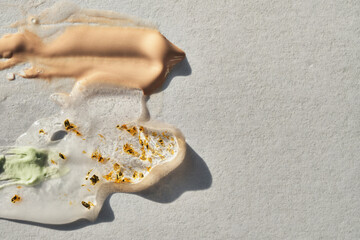 Various cosmetic products and shimmering gold foil on light gray background