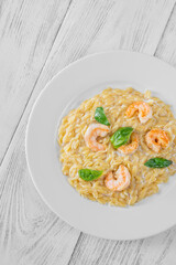Creamy orzotto pasta topped with grilled prawns and fresh basil on rustic wooden table