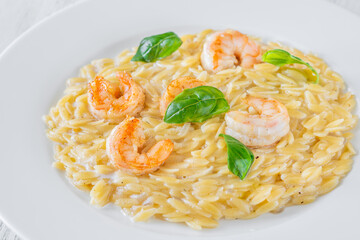 Creamy orzotto pasta topped with grilled prawns and fresh basil on rustic wooden table