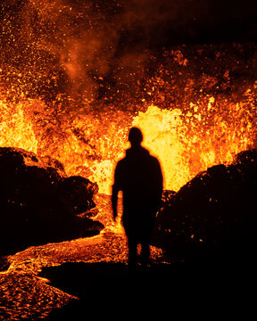 Aerial view of a lone figure stands silhouetted against the fiery spectacle of erupting lava, a mesmerizing dance of destruction and awe, Reykjavikurborg, Iceland.