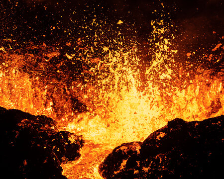 Aerial view of molten lava erupting and splashing, contrasting the dark rock formations with the bright, fiery orange hues, Reykjavikurborg, Iceland.