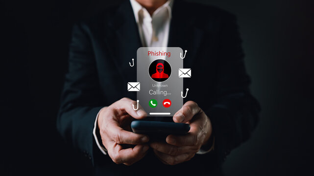 Businessman holding smartphone with phishing call warning icon. Concept of cyber security, scammer fraud, identity theft risk, and mobile technology digital safety protection.