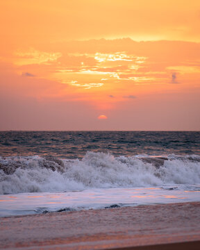 View of waves crashing onto the sandy beach under a fiery orange and pink sky as the sun dips below the horizon, Mirissa, Southern Province, Sri Lanka.