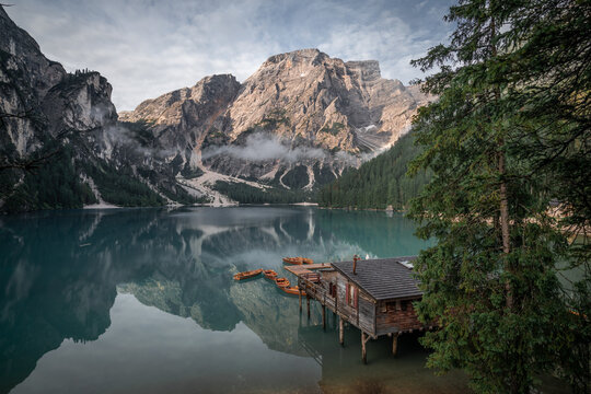 View of the Braies Lake reflecting the mountains, a wooden house, and the forest under a cloudy sky, lago di braies, Trentino-South Tyrol, Italy.