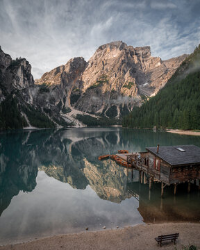View of tranquil lake mirroring majestic mountains under a sweeping sky, a rustic boathouse adding charm to the serene landscape, Lago di Braies, Trentino-South Tyrol, Italy.