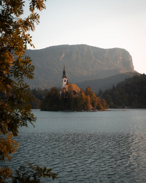 View of a solitary church standing proudly on an islet in the middle of the lake, framed by verdant trees and a majestic mountain backdrop, Bled, Radovljica, Slovenia.